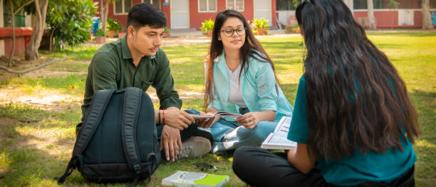 Small group of Asian/Indian university students sitting in a campus ground studying together and discussing on a book. Panoramic image with copy space.